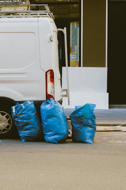 In the image, a large pile of mixed waste materials is placed outdoors on a paved driveway or loading area. The waste includes various items such as cardboard boxes, plastic containers, and miscellane