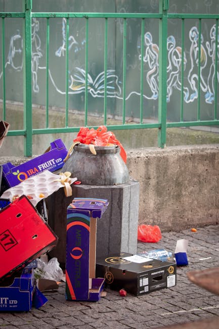 A person wearing a red hooded jacket is kneeling on a dark, textured surface, facing a large, vibrant graffiti mural that features bold red, orange, and purple lettering with some blue and black accen